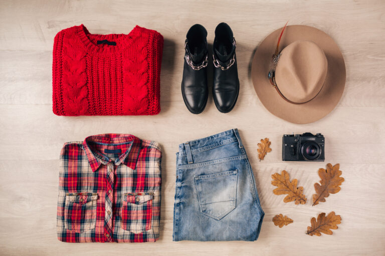 flat lay of woman style and accessories, red knitted sweater, checkered shirt, denim jeans, black leather boots, hat, autumn fashion trend, view from above, vintage photo camera, traveler outfit